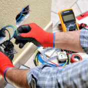 Electrician wearing safety gloves inspecting exposed outlet wires during emergency electrical repair