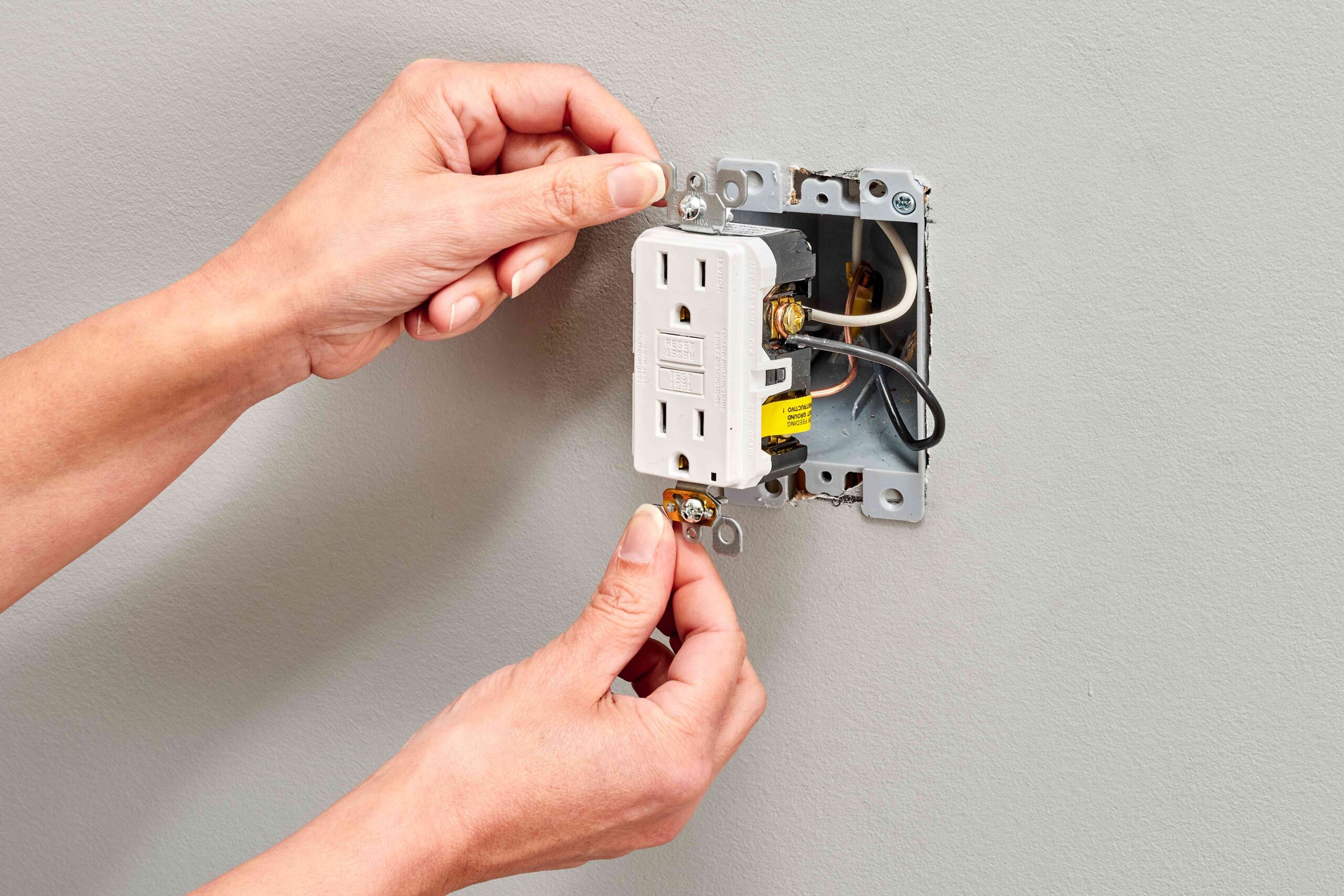 Electrician installing and repairing a GFCI outlet with exposed wiring in a residential home