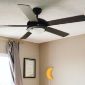 Modern black ceiling fan installed in a Seattle living room with textured ceiling and curtain windows