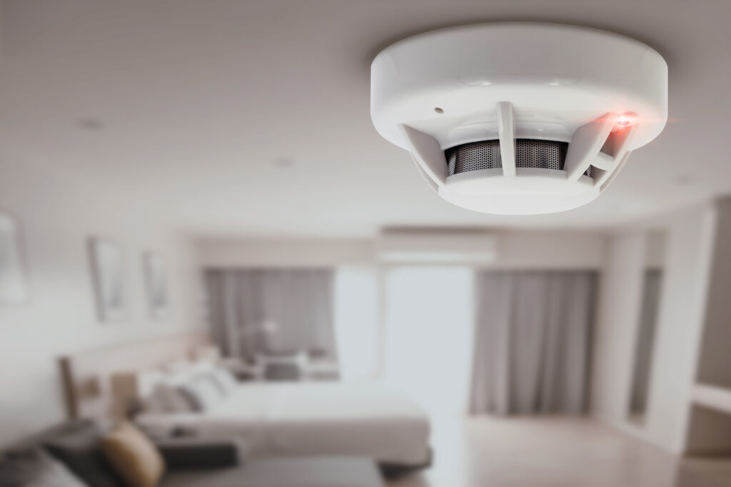 Smoke detector installed on a bedroom ceiling with red indicator light, ensuring home safety by Surge Electrical in the Puget Sound area.